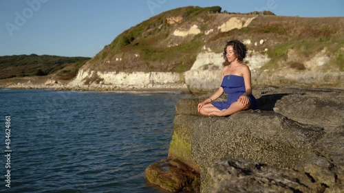 Relaxed woman sitting on a rock against the sea and meditating. Yoga Meditation Outdoor at Sunrise, Zen State. photo