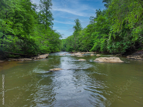 an aerial shot of the running waters of Big Creek River surrounded by miles of lush green trees and plant with rocks on the banks of the river and gorgeous sky at Vickery Creek in Roswell Georgia photo