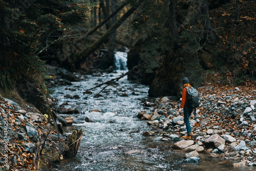 woman in the mountains near the river with a backpack on her back and a forest in the background