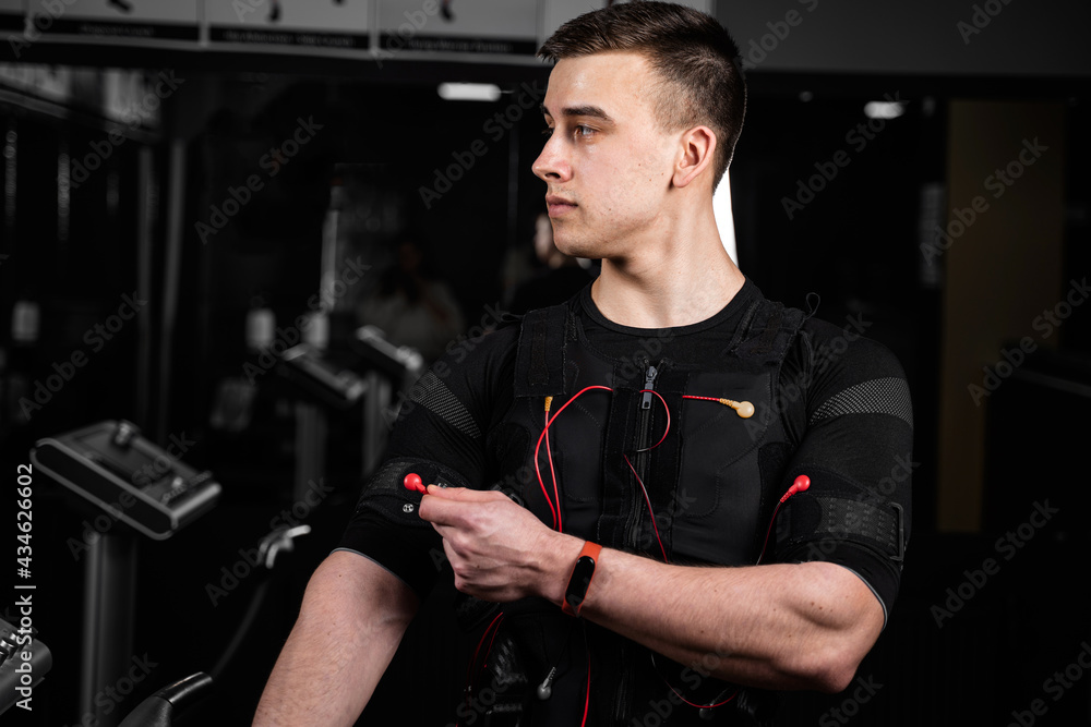 Handsome trainer in EMS suit with red wires for electro impulse stimulation for body. Training in gym. Handsome trainer in EMS suit with red wires for electro impulse stimulation for body. Training in gym.