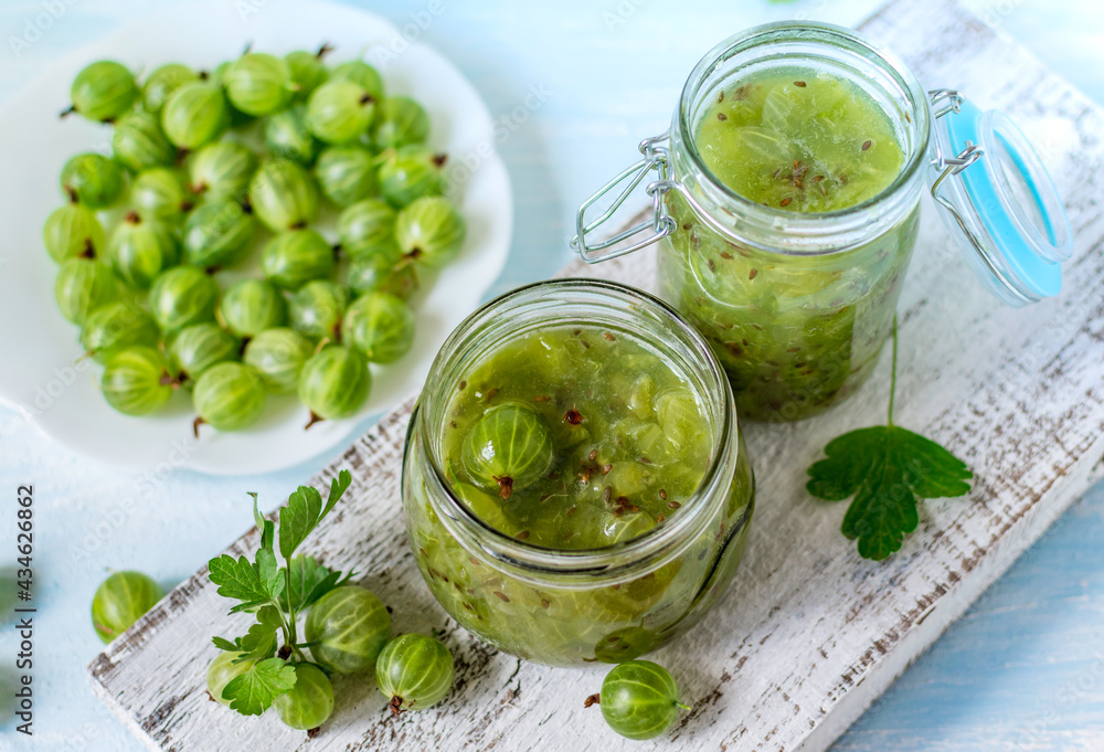 A small glass jar with homemade jam and the fresh gooseberry berries on a white background. Selective focus. A small glass jar with homemade jam and the fresh gooseberry berries on a white background. Selective focus.
