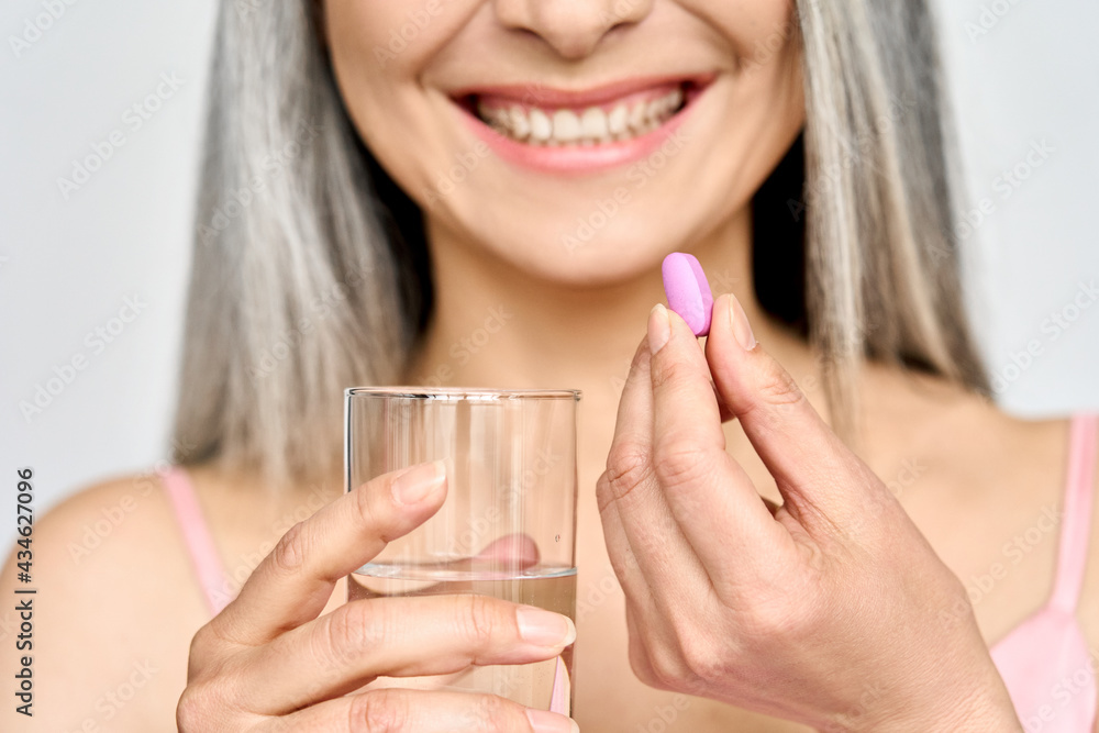 Crop closeup portrait of smiling happy middle age Asian woman with glass of water and vitamins collagen calcium pill taking care of face body and hair health and wellness everyday. Crop closeup portrait of smiling happy middle age Asian woman with glass of water and vitamins collagen calcium pill taking care of face body and hair health and wellness everyday.