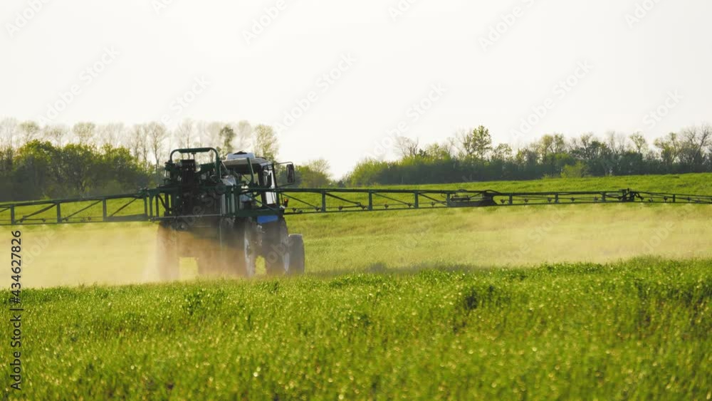 Spraying a green wheat field by tractor. The farming tractor spraying on field with sprayer, herbicides and pesticides. Industrial machine fertilizing a field. Chemicals used by agricultural tractor. Spraying a green wheat field by tractor. The farming tractor spraying on field with sprayer, herbicides and pesticides. Industrial machine fertilizing a field. Chemicals used by agricultural tractor.