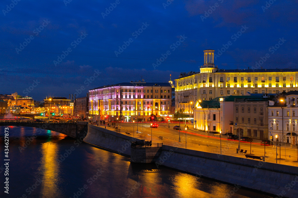 Fototapeta premium A bright blue evening in Moscow with a view of the river, Yakimanskaya embankment and old houses in the light of evening lamps.