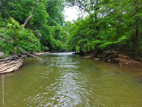 an aerial shot of the running waters of Big Creek River surrounded by miles of lush green trees and plant with rocks on the banks of the river and gorgeous sky at Vickery Creek in Roswell Georgia photo