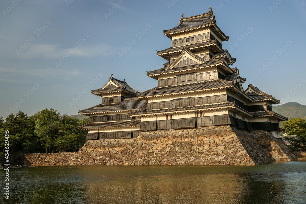 Matsumoto Castle, known as The Crow Castle facade covered in sunshine at sunset, surrounded by a water moat. Matsumoto, Japan. Matsumoto Castle, known as The Crow Castle facade covered in sunshine at sunset, surrounded by a water moat. Matsumoto, Japan.
