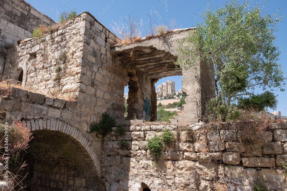 Ruins of buildings in Lifta, a depopulated Palestinian Arab village on the outskirts of Jerusalem. National nature reserve Lifta. A high-rise building of the modern Jerusalem on the background