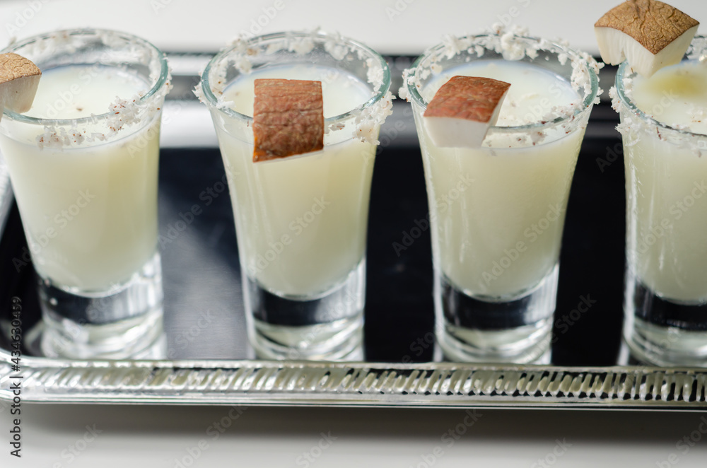 Coconut cocktail in drink shot glass based on the rum decorated with coconut flakes served on a silver tray Coconut cocktail in drink shot glass based on the rum decorated with coconut flakes served on a silver tray