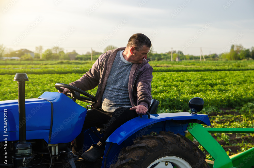 Fototapeta premium A farmer drives a tractor while harvesting potatoes. First potato harvest in early spring. Agro industry and agribusiness. Harvesting mechanization in developing countries. Farming and farmland.
