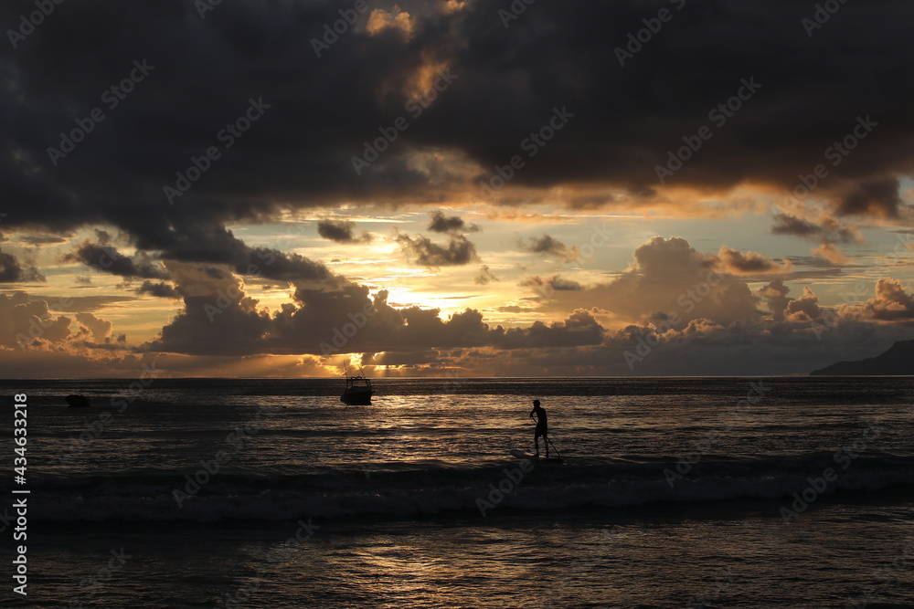 Night image of the silhouette of a surfer on a board in the sea at sunset.Beautiful seascape with the golden sun sinking into the black clouds on the horizon
