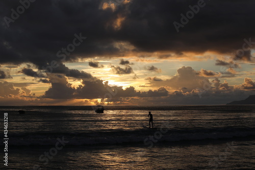 Night image of the silhouette of a surfer on a board in the sea at sunset.Beautiful seascape with the golden sun sinking into the black clouds on the horizon