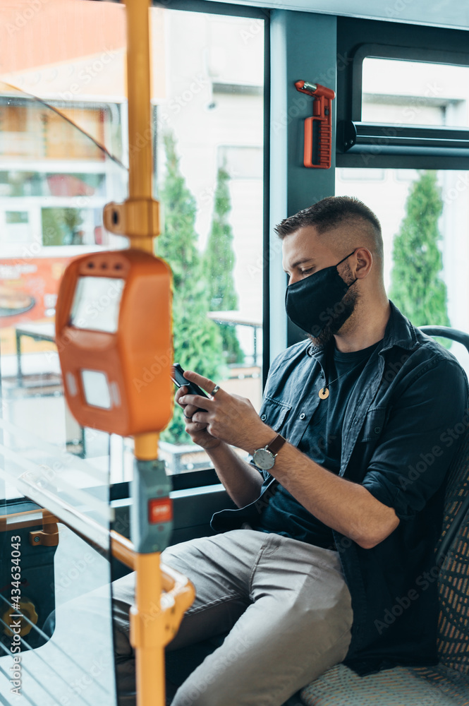 Man wearing protective mask and using a smartphone while riding a bus