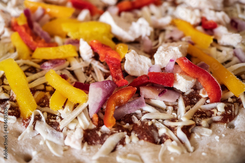 Frozen pizza with chicken pieces, red and yellow peppers ready to be cooked. Fast food concept. Retail industry product. Selective focus, close up