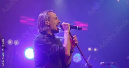 Expressive singer singing into microphone. Live music concert in front of bright colorful strobing lights on stage. Slow motion