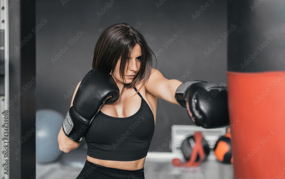 Medium shot of girl practicing boxing with a red bag. she is concentrated and hitting the bag intensely.
