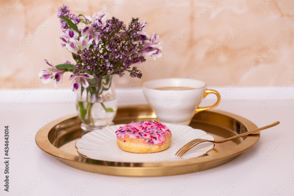 Coffee cup and sweet strawberry donut on golden plate with flower bouquet Coffee cup and sweet strawberry donut on golden plate with flower bouquet
