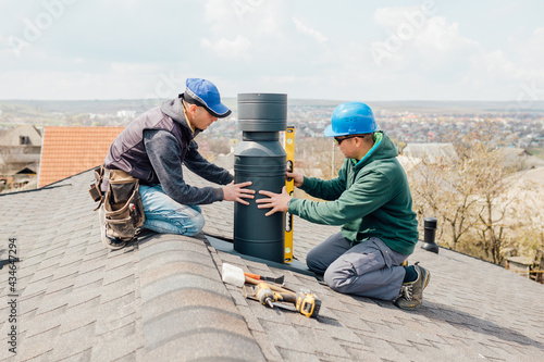 workers on the roof installing tin cap on the iron chimney. roofing Construction and Building New iron House with Modular Chimney,
