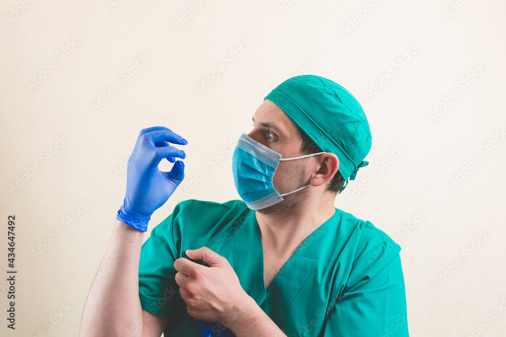 Young doctor with blue glove on hand in green surgeon suit and protective breathing mask isolated Young doctor with blue glove on hand in green surgeon suit and protective breathing mask isolated