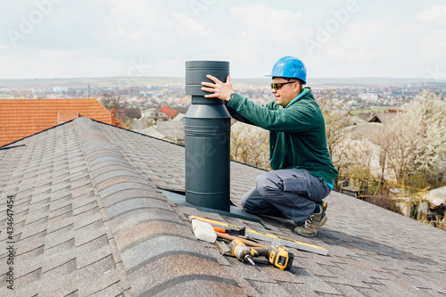 worker with blue helmet on the roof installing iron chimney. roofing Construction and Building New iron House with Modular Chimney. photo