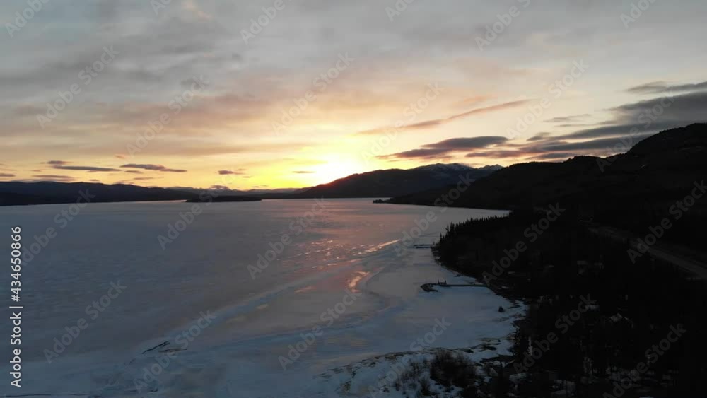 Drone aerial view of sunset over a frozen lake in northern Canada, Yukon Territory during spring time with wilderness surrounding the stunning landscape. Drone aerial view of sunset over a frozen lake in northern Canada, Yukon Territory during spring time with wilderness surrounding the stunning landscape.