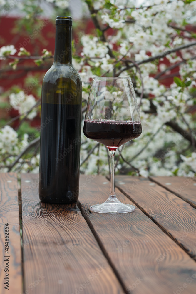 A half-filled glass and a bottle of red wine on a background of cherry blossoms.