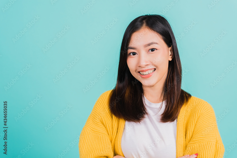 Young Asian beautiful woman smiling wear silicone orthodontic retainers on teeth with crossed arms, studio isolated on blue background, retaining tools after removable braces. Dental hygiene concept Young Asian beautiful woman smiling wear silicone orthodontic retainers on teeth with crossed arms, studio isolated on blue background, retaining tools after removable braces. Dental hygiene concept