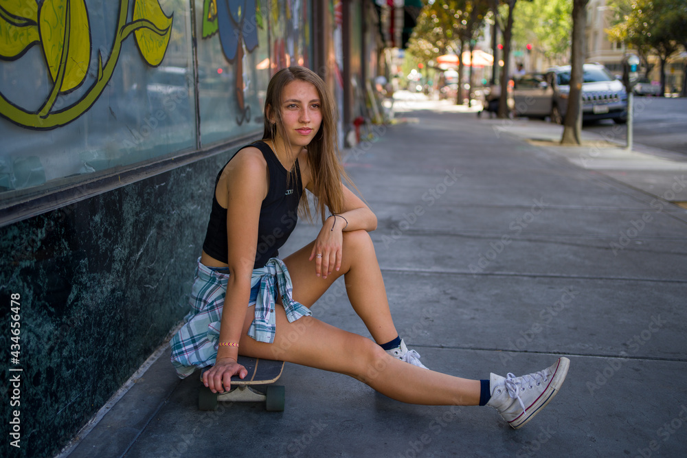 Young Woman Seated With Skateboard on the Sidewalk in a Downtown Area