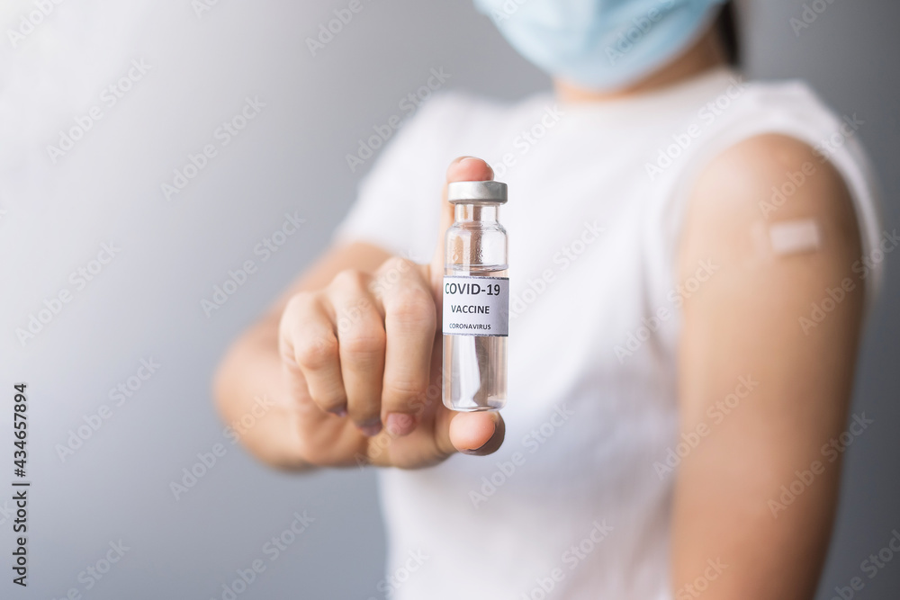 Happy Woman showing COVID-19 vaccine vial and her arm with bandage after receiving vaccination. immunization, inoculation and Coronavirus pandemic Happy Woman showing COVID-19 vaccine vial and her arm with bandage after receiving vaccination. immunization, inoculation and Coronavirus pandemic