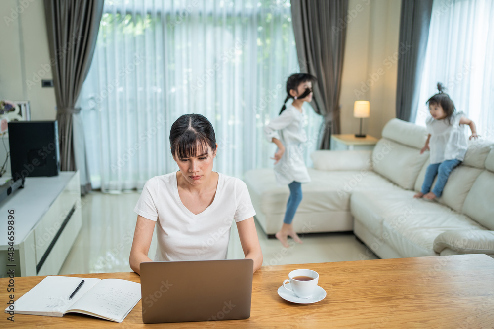 Asian mother working at home, getting disturb by kids playing around.