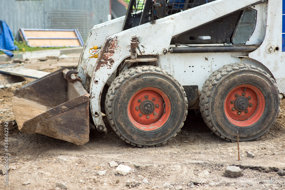 Fototapeta premium Mini excavator at a construction site loads the ground with a front bucket, close-up