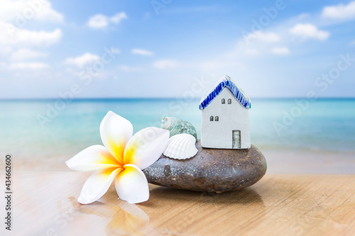 Summer beach house  vintage style ceramic house on stone and seashell with plumeria flower over blurred beach background  summer concept