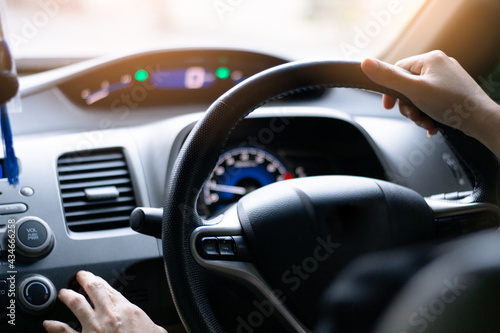 A woman sitting in front of the driver in a black car, using her fingers pressing a function button on the console inside the car, traveling on the road, © Thassanee