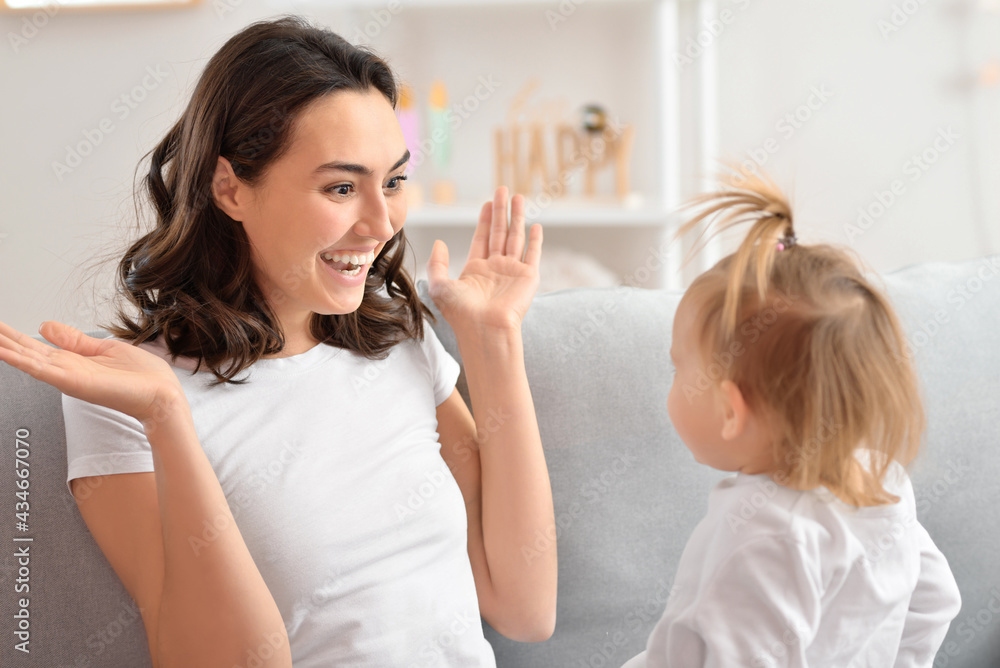 Happy woman and her little daughter playing on sofa at home