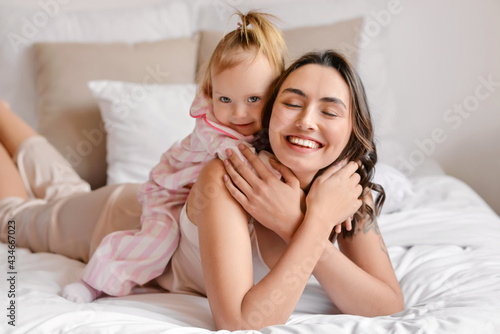 Happy woman and her little daughter lying on bed at home