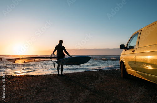 Surfer on the background of a colorful sunset and a surfmobile 
