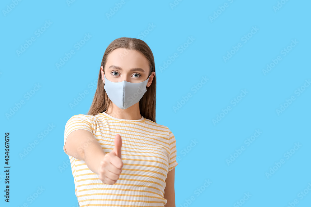 Stylish young woman wearing mask and showing thumb-up on color background Stylish young woman wearing mask and showing thumb-up on color background