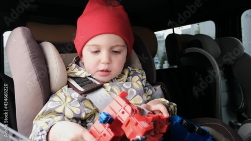 Child in hat and jacket plays with robot sitting in car