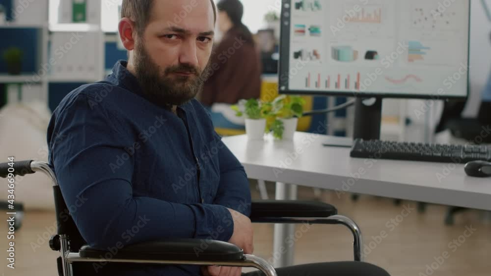 Young man with disabilities, invalid, handicapped disabled paralized immobilized looking at camera upset, tired sitting in wheelchair in business office room, working at financial project with team. Young man with disabilities, invalid, handicapped disabled paralized immobilized looking at camera upset, tired sitting in wheelchair in business office room, working at financial project with team.