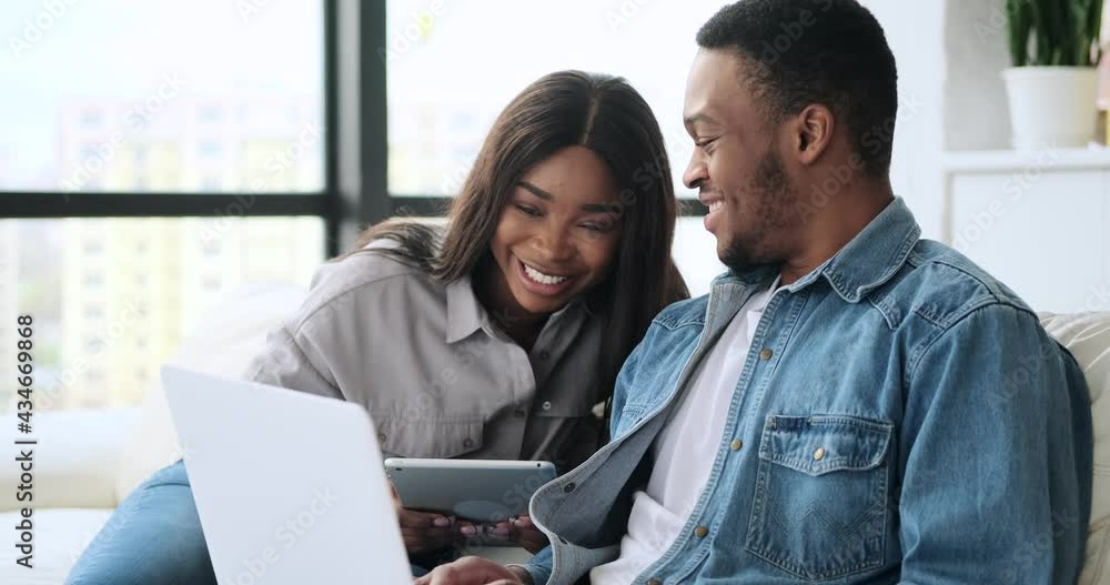 Woman using digital tablet talking with husband working on laptop at home Woman using digital tablet talking with husband working on laptop at home