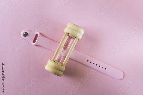 hourglass with a pink silicon wristband from smartwatches on a pink surface 