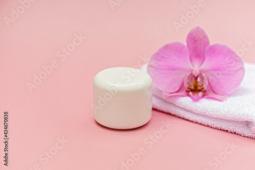 Jar of moisturizing body cream  bath towel  orchid flower on a pastel pink background. Skin care cosmetic concept. Soft selective focus. Copy space.