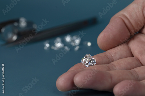 Foto Cut diamond in hand close up with jewelry tools and scattering of different diamonds in background, front view on blue background