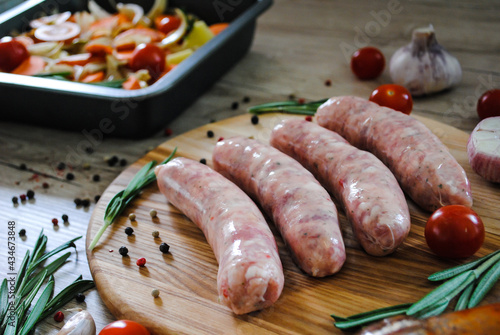 Raw pork sausages with spices on a cutting board on a wooden background.