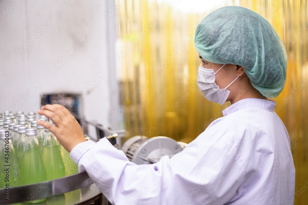 Female worker inspecting quality control for juice drink product on bottling factory machinery. Process of beverage industrial production Female worker inspecting quality control for juice drink product on bottling factory machinery. Process of beverage industrial production