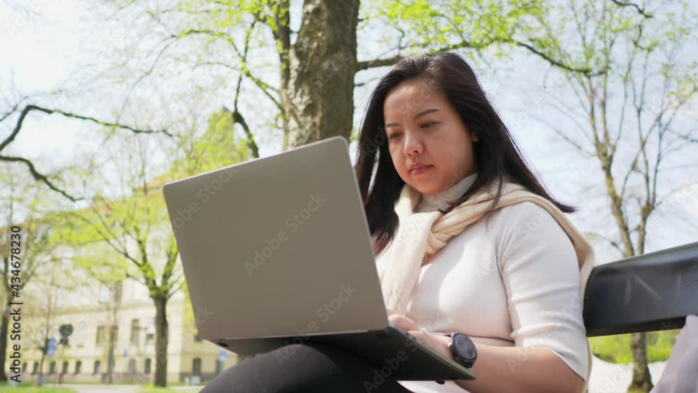 Asian black straight hair woman sitting on a chair and spending time to work on laptop at park. Working outside, feeling relaxed and happy with greenfield Asian black straight hair woman sitting on a chair and spending time to work on laptop at park. Working outside, feeling relaxed and happy with greenfield