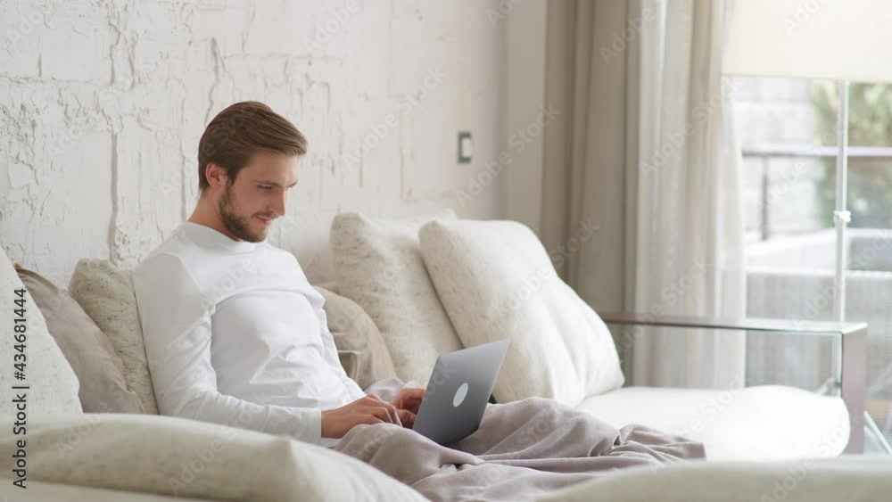 Cheerful caucasian man sits at home on the couch and works using a laptop, financial manager on a remote work during self-isolation in quarantine, a man makes good deal, positive emotions. Cheerful caucasian man sits at home on the couch and works using a laptop, financial manager on a remote work during self-isolation in quarantine, a man makes good deal, positive emotions.