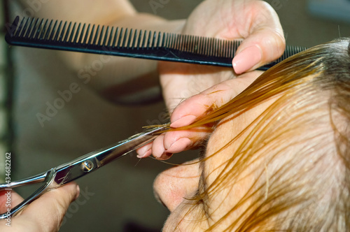 close-up - a hairdresser cuts a woman with blond short hair, holding scissors and a comb