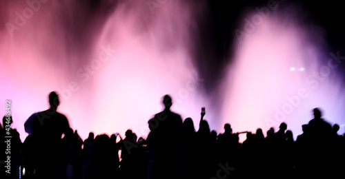 Silhouettes of people in motion near a colored fountain at night.