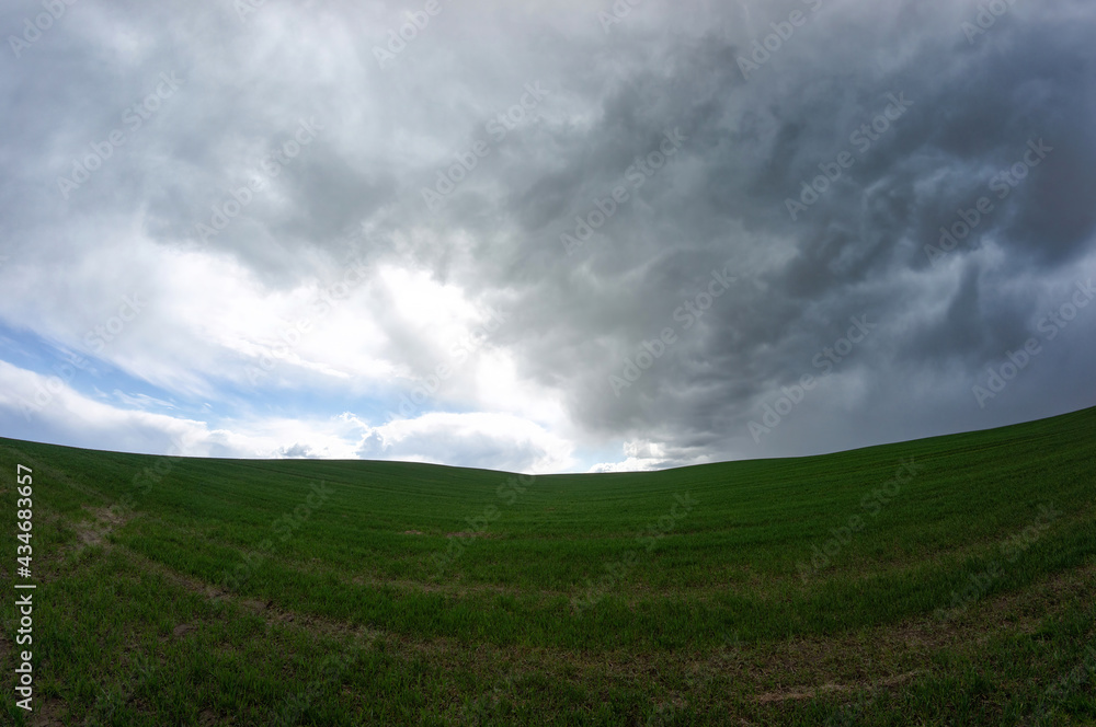 Dark thundercloud approaching the blue sky over the green field Dark thundercloud approaching the blue sky over the green field