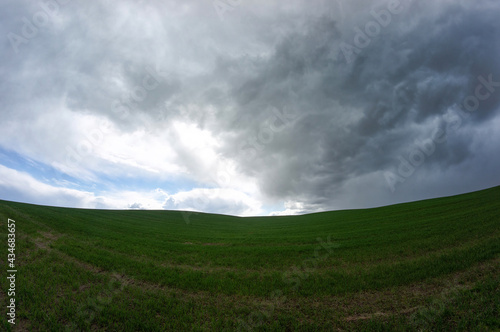 Dark thundercloud approaching the blue sky over the green field